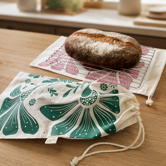A patterned fabric drawstring bag and a matching cooling mat with a rustic loaf of bread on a wooden table in a kitchen setting.